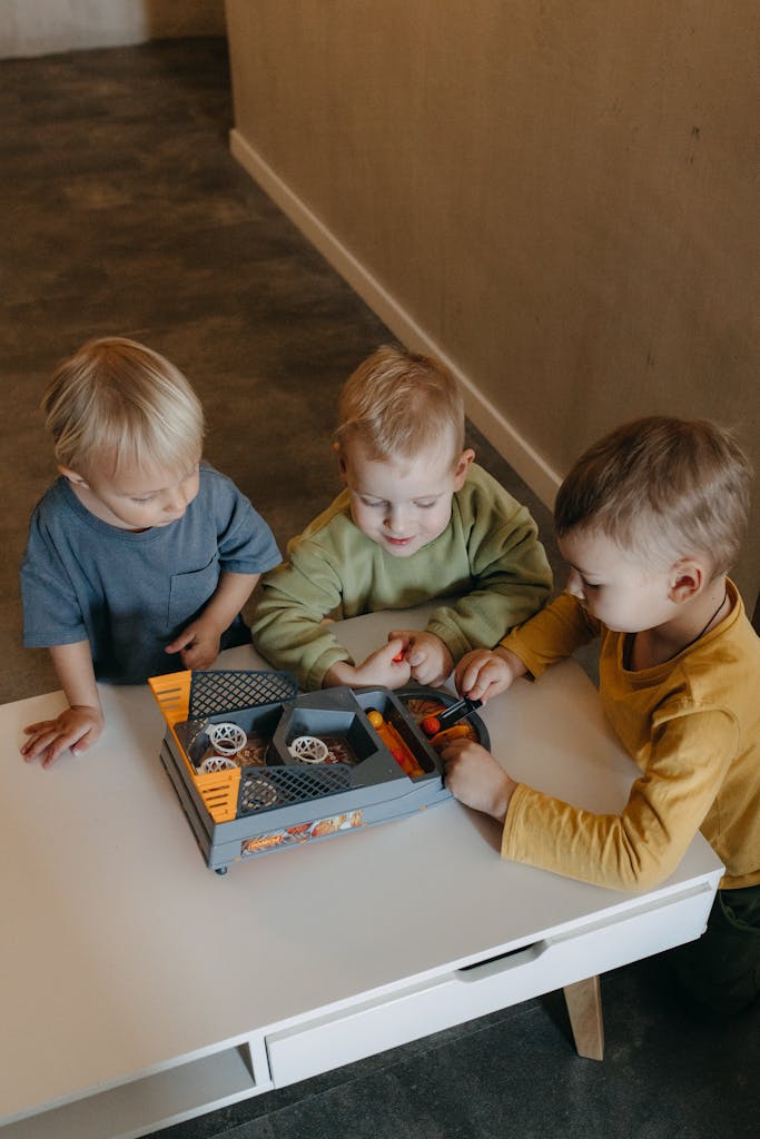 Three toddlers engaged in play with toy car on a table inside a room.